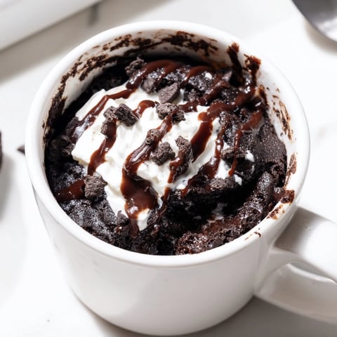 Warm Oreo Mug Cake, ready to enjoy, topped with whipped cream and crushed cookies.