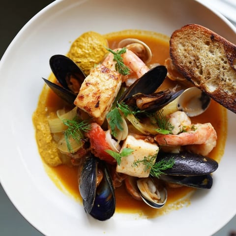 Steaming, flavorful bouillabaisse: a vibrant, aromatic seafood stew served alongside crusty bread with rouille.
