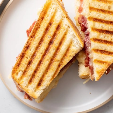 A golden-brown Crispy Prosciutto & Fig Panini sliced to reveal layers of melted cheese, salty prosciutto, and sweet fig jam.