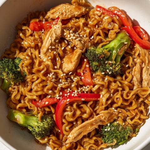 Steam rises from a sizzling pan of Spicy Ramen Stir-Fry, loaded with tender chicken, crisp broccoli, and vibrant red bell peppers.