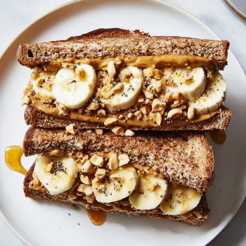 Golden peanut butter and banana sandwich with honey drizzle, chopped peanuts, and granola ready to serve.