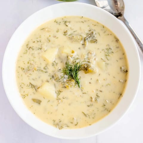 A close-up view of a steaming bowl of Creamy Dill Pickle Soup, garnished with fresh dill sprigs.