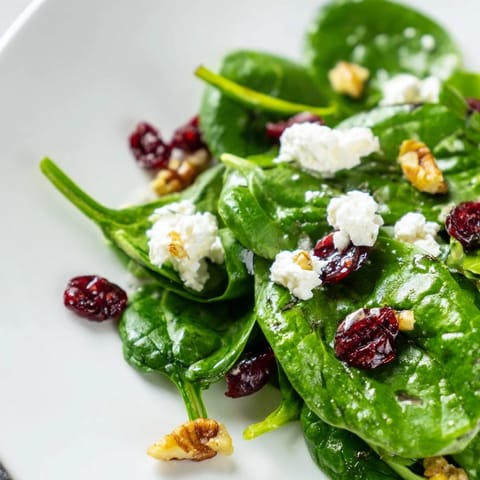 Vibrant bowl of Spinach Goat Cheese Salad featuring tender greens, rich goat cheese, and candied pecans, dressed for a light lunch or starter.