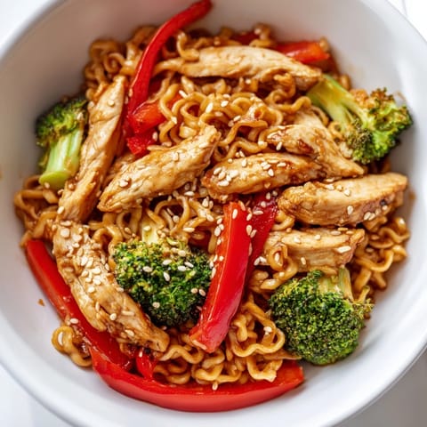 A close-up of Spicy Ramen Stir-Fry showcases glossy noodles tangled with fresh vegetables and a garnish of toasted sesame seeds.