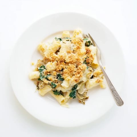 A close-up of a serving of Artichoke Pasta Bake on a white plate, showing tender pasta and vibrant green spinach in rich sauce.