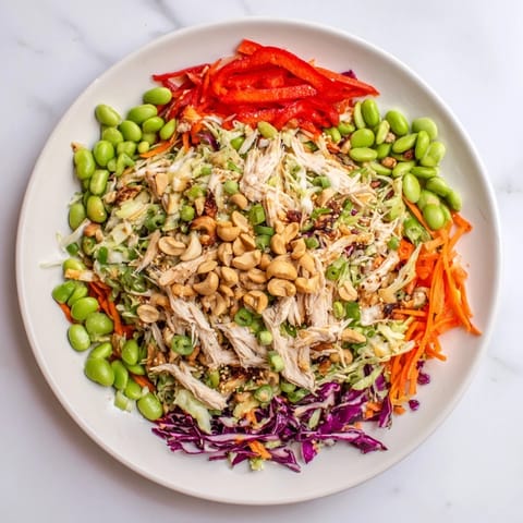 The completed Edamame Crunch Chicken Salad garnished with toasted sesame seeds and cashews, served on a rustic wooden table with a fresh, appetizing look.