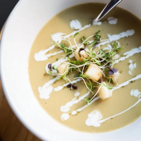 Silky smooth Celery Root Bisque in a rustic ceramic bowl, topped with microgreens and a drizzle of truffle oil.