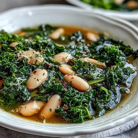 A steaming bowl of kale and white bean soup with lemon and garlic, garnished with fresh parsley and a lemon wedge.
