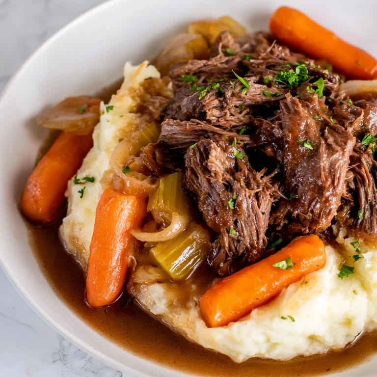 A close-up of a steaming bowl of slow cooker pot roast, rich gravy, and fluffy mashed potatoes.