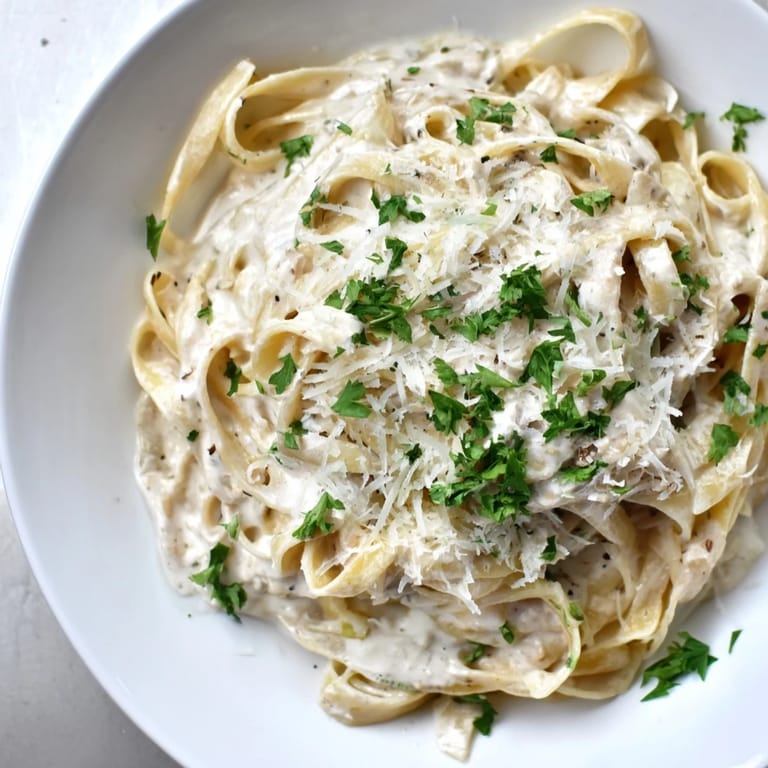 A steaming bowl of Skinny Alfredo Garlic Parmesan Snowy Pasta topped with fresh green parsley.