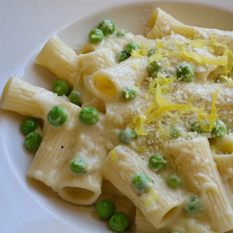 A close-up of pea and lemon ricotta pasta showing creamy sauce clinging to al dente rigatoni and bright green peas.  