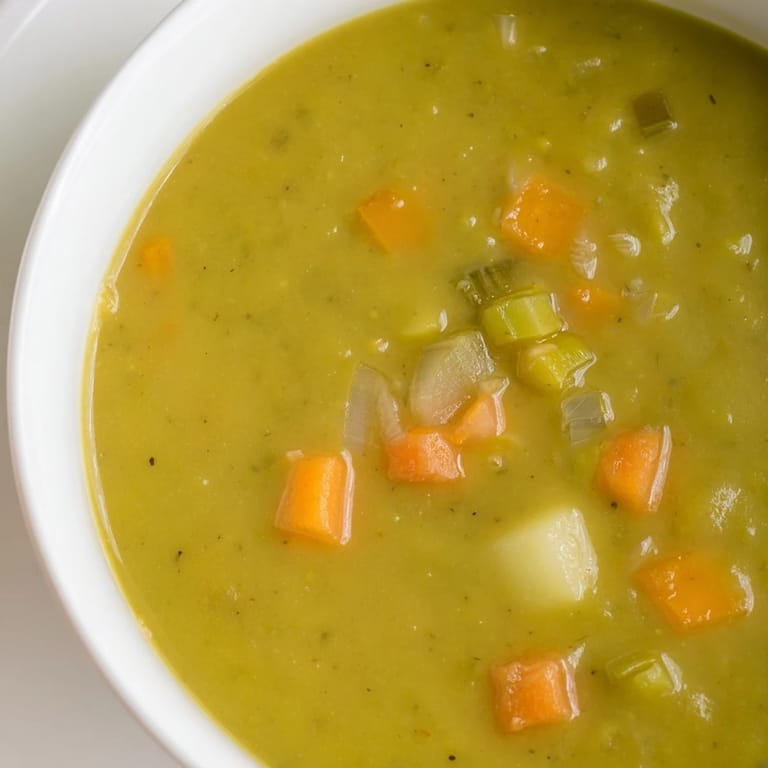 Hearty split pea soup with diced potatoes and carrots, served steaming hot in a ceramic bowl.