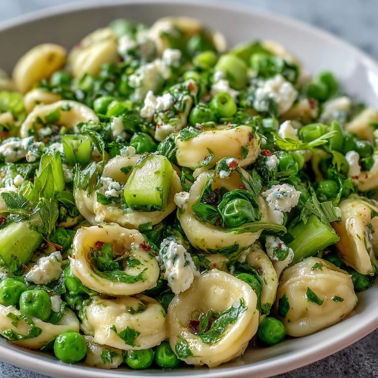 A close-up of Fresh Spring Pea and Mint Pasta Salad with Lemon Vinaigrette, showcasing vibrant peas and herbs in a garden setting.