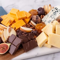 A rustic Fireside Comfort & Cocoa platter piled high with cheeses, chocolates, and fruits.