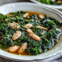 A steaming bowl of kale and white bean soup with lemon and garlic, garnished with fresh parsley and a lemon wedge.